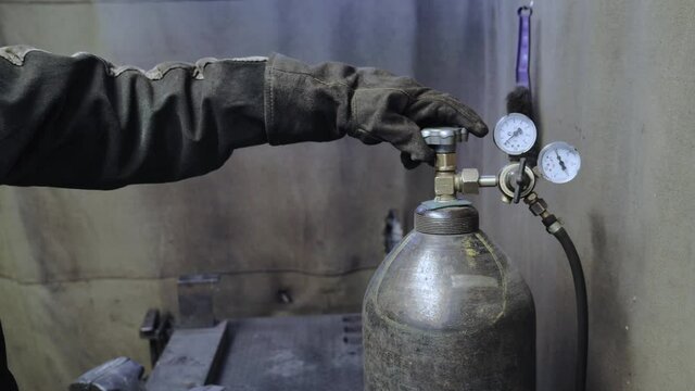 A worker in the workshop opens the valve of the oxygen or gas tank. Worker in a protective gloves. 