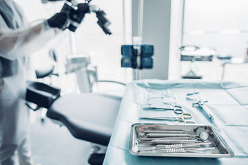 Sterile surgical instruments against background of nurse preparing medical equipment for dental surgery operation