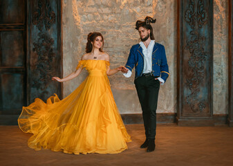 Couple walks in room old castle. Happy beauty woman fantasy princess in yellow dress and guy enchanted beast, horns on head. Romantic male prince holding hand. Man monster carnival blue king costume © kharchenkoirina