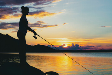 Mom and her little daughter are fishing with a fishing rod on a pier at sunset by the lake