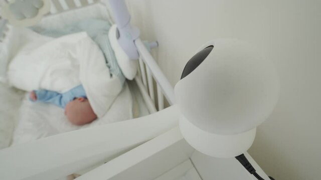 Ip camera as baby monitor camera above the crib in the bedroom, newborn baby boy is sleeping peacefully in bed. High quality 4k footage