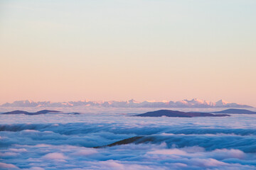 Naklejka na ściany i meble View of the High Tatras in Slovakia, which rise above the clouds and are covered with snow. View from Lysa Hora. Sunset with snowy hills. The sea of clouds floats in the wind