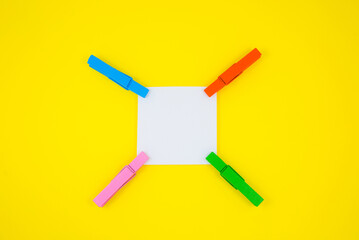 Blank white To Do List Sticker with colorful wooden clothespins. Close up of reminder note paper on the yellow background. Copy space. Minimalism, original and creative photo.