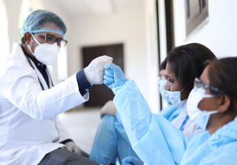 Shallow focus of South Asian health workers in protective suits doing a fist bump
