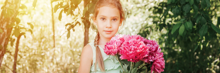Naklejka premium portrait of a happy cute little caucasian seven year old kid girl in light green sundress, holds in hands a bouquet of pink peony flowers in full bloom on the background of nature. banner. flare