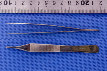 Adson plain forceps on a blue background
