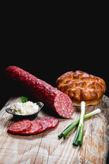 Dry meat sausage on a wooden plate with vegetables