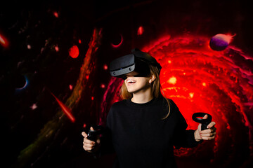 The girl happily and emotionally plays the game in virtual reality glasses holding gamepads in her hands. Red game background
