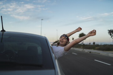 A Caucasian female cheerfully leaning out through her car window