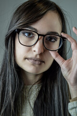 Portrait of a beautiful young woman with long brown hair adjusting her eyeglasses