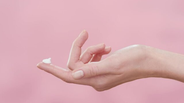 Female skincare model lifts her hand with a blob of cream on forefinger up against pink ripple background | Skincare cream commercial