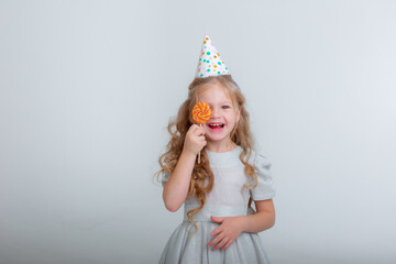 little girl in a birthday hat with a lollipop on a white background studio