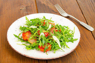 Dish of arugula, tomatoes, dried meat and cheese. Salad on plate on wooden background