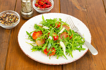 Dish of arugula, tomatoes, dried meat and cheese. Salad on plate on wooden background