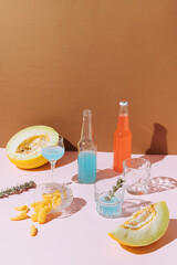 Summer , party scene with two bottles of cocktails, melons, glasses and snacks against pink , brown background.Minimal Summer concept.