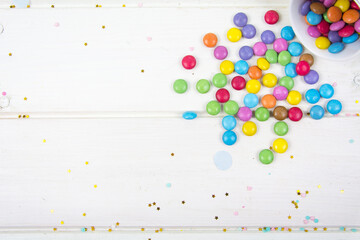 Colored candy bonbons scattered on white wooden board background