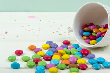 Colored candy bonbons scattered on white wooden board background