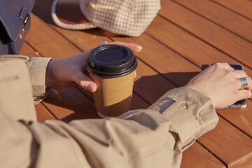 A woman in a street cafe with a cardboard cup in her hands.