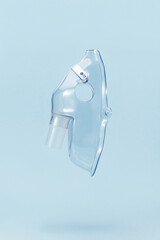 Transparent respiratory mask for compressor nebulizer flying on blue background. Medical equipment for inhalation therapy for asthma and respiratory diseases.