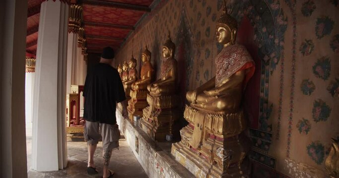 Male Tourist Walking Along the Hall in Wat Arun Temple Passing Through Golden Buddha Statues