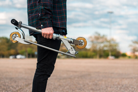 Un hombre joven sosteniendo un patinete no el&eacute;ctrico plegado de aluminio