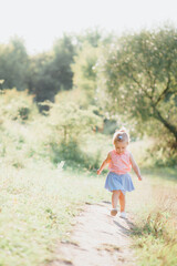 little girl 2-3 years old European appearance. the child walks on a path near the forest. blonde hair. green forest and grass. sunny day.