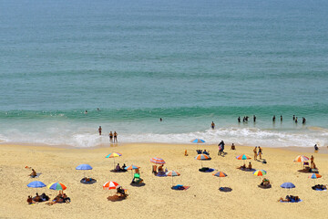 Fototapeta na wymiar People under umbrellas on a paradise beach. Sunny vacation by the ocean. Top view of a sandy beach.