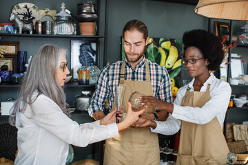 Mature woman choosing decor at modern store and consulting with two multiracial workers. Professional sellers in uniform providing service for customer.