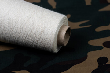Fototapeta na wymiar bobbin with white thread on camouflage fabric. Close-up