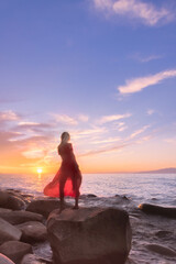 silhouette of  blondy lady in red dress at sunset at shore of sea