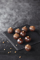 Handmade Chocolate Glazed Truffles, decorated with caramelized walnuts, on a black board, on a dark gray background.