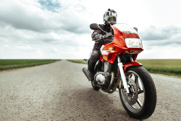 Man rides a red motorcycle on a country road