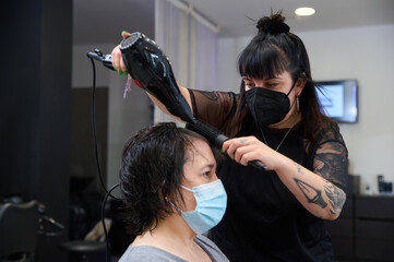hairdresser with mask drying the client's hair with hairdryer