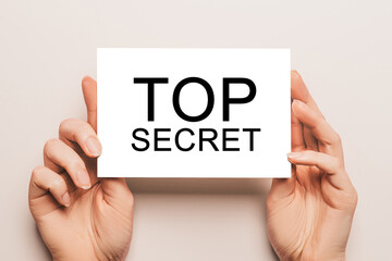 Female hands hold card paper with text Top Secret on a yellow background. Business and finance concept