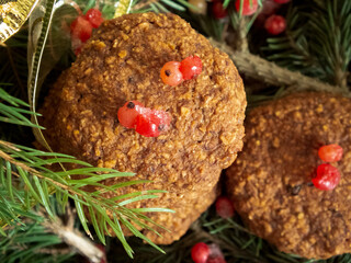 Fototapeta na wymiar Christmas cookies with red berries, next to a yellow holiday bow, on a background of fir branches