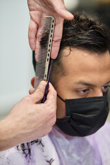 hairdresser cutting hair of client with mask