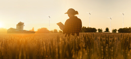 Farmer in a wheat field. Wind turbines in the field. Clean energy.