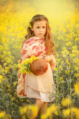 Naklejka na ściany i meble Cute little girl with a basket in a blooming canola field.