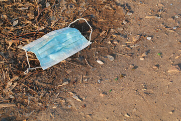 a used disposable medical mask thrown on the ground like rubbish among stones and glass, medical trash on public streets, a social problem of environmental pollution