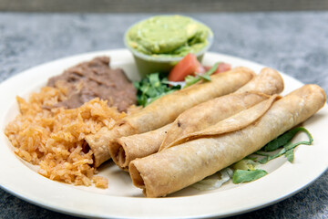 Tradional comibination plate of tasty Mexican food consisting of taquitos, rice, and refried beans.
