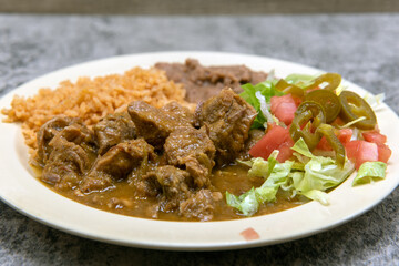 Authentic Mexican food plate of chili verde pork smothered in green sauce served with refried beans and rice.