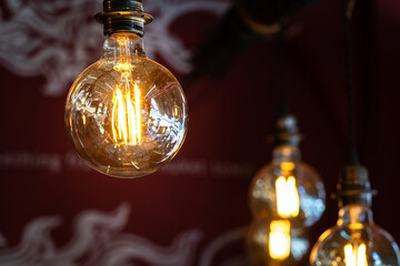 A classic style ceiling light bulb which is glowing in orange warm lighting shade. Interior object for room decoration. Close-up and selective focus.