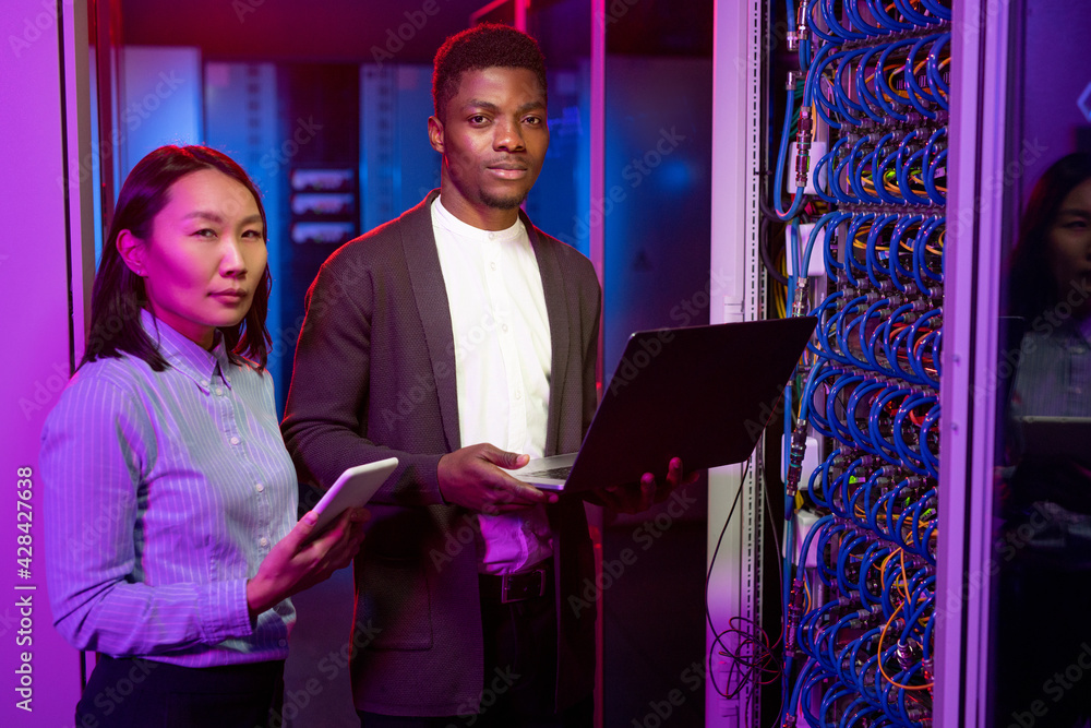 Poster multi-ethnic it engineers with gadgets in server room