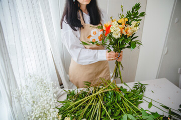 a young brunette woman in an apron in the process of creating a bouquet in the rustic style in her flower shop