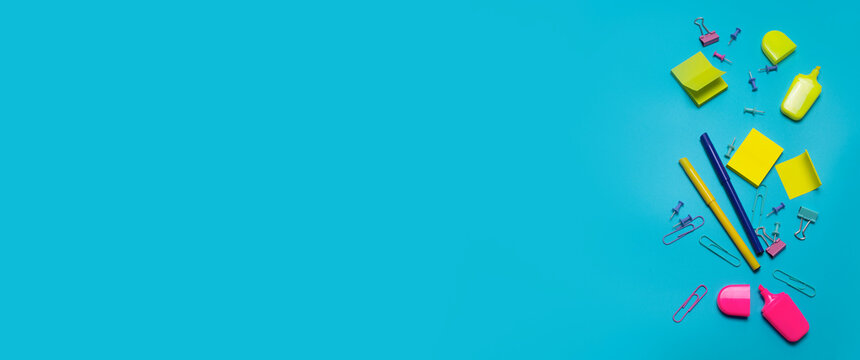 Stationery items on the blue background with free space for text. Creative, colorful background with scool or office supplies. Flatlay with copy space, top view. Markers, paper clips, sticky notes.