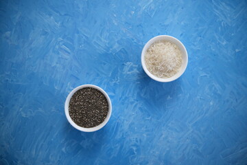 Rice and chia seeds are organic food for a healthy diet. In a round bowl. Two white cups. The blue background is painted with oil paints.