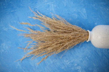 The composition consists of a white ceramic vase with a bouquet of dried spikelets, a golden photo frame with a dried flower on a blue background painted with oil paints. Stylish home decor