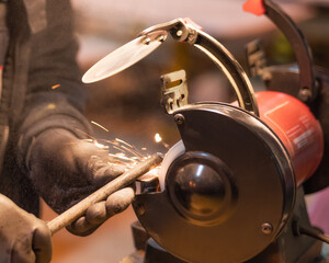 A mechanic in a gray jumpsuit processes a metal part on a grinding machine
