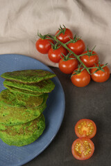 spinach and zucchini pancakes lie on a beautiful blue plate, decorated with a cherry tomato sprig, which lie on a cotton napkin. on a dark background