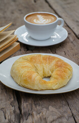 Cappuccino with beautiful latte art and croissant on wooden background on the table. Perfect breacfast in the morning. Rustic style.